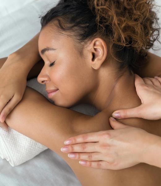 African-american woman enjoying shoulder massage, lying with closed eyes in spa center